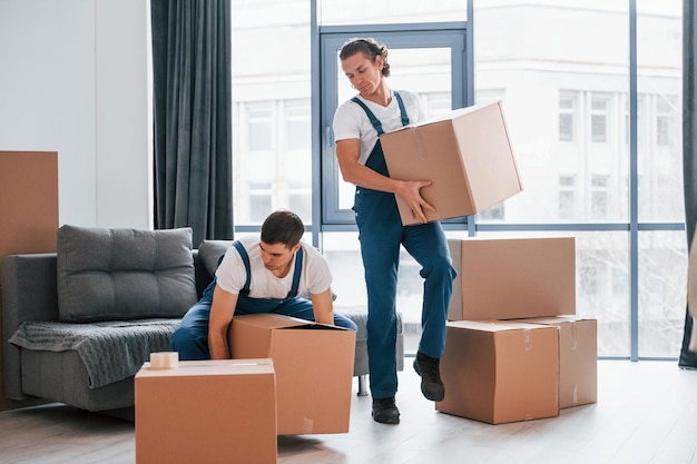 忙しい日部屋の中で屋内で働く青い制服を着た2人の若い引っ越し業者