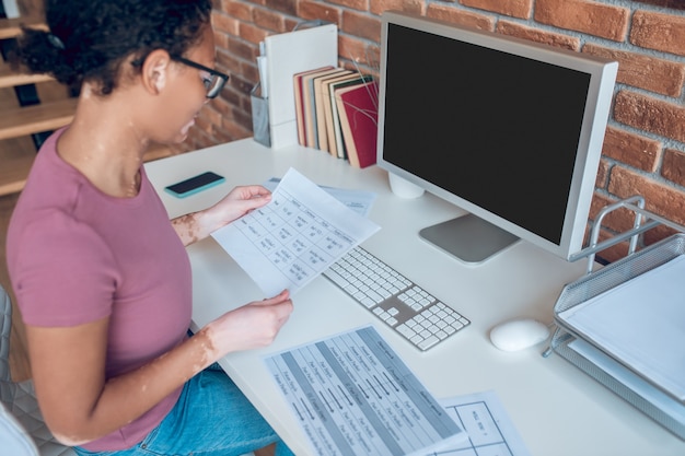 A busy day. A woman in eyeglasses working on a computer and looking busy