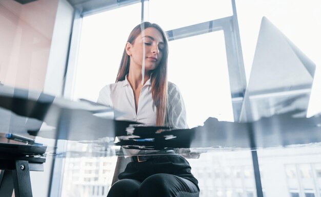 Busy day Young woman in white formal clothes is indoors in the modern office