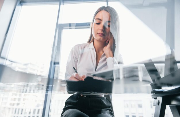 忙しい日白いフォーマルな服を着た若い女性が現代のオフィスの屋内にいます