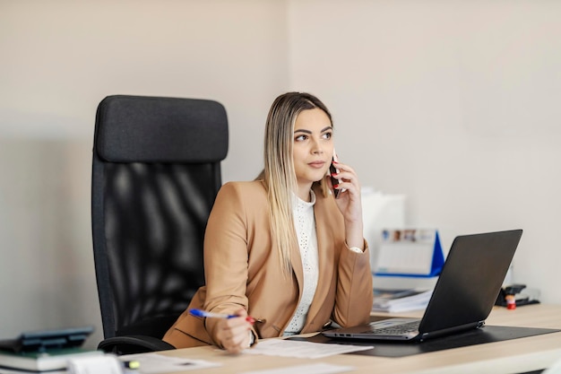 A busy female CEO is sitting in her office and having important phone call with business partner