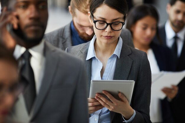 Busy lady reading document on tablet while standing in line