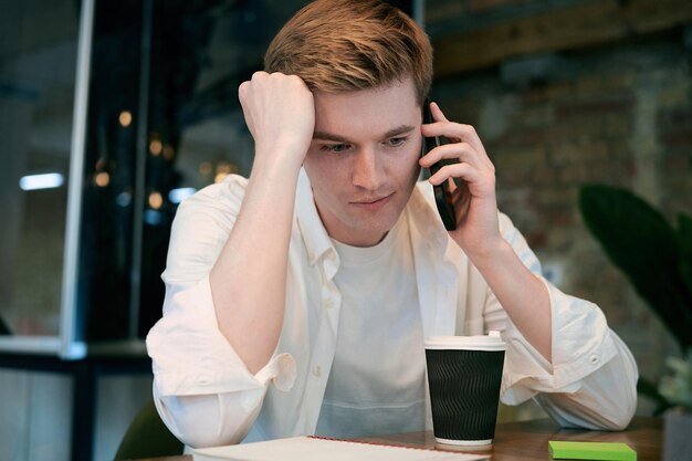 Busy male coworker uses smartphone while talking at desk in office Startup coworking concept