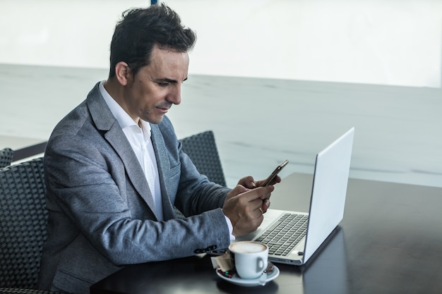 Busy male entrepreneur working with laptop and smartphone in cafe