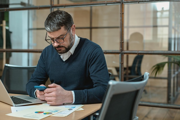 Busy man in glasses typing on smartphone in the office