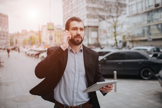 L'uomo impegnato ha fretta, non ha tempo, parlerà al telefono mentre è in movimento. uomo d'affari che fa più compiti. uomo d'affari multitasking.