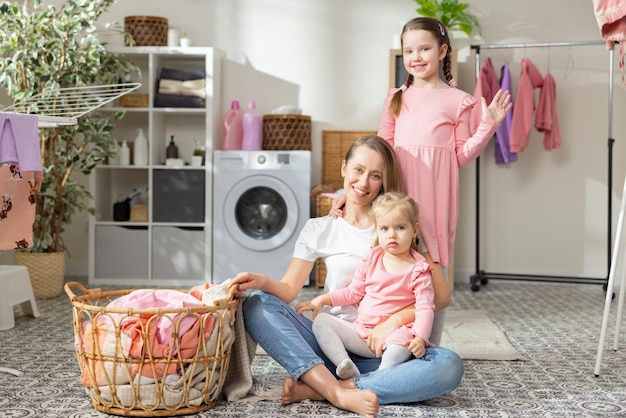 A busy mom with two daughters spends time in the laundry room\
while doing household chores