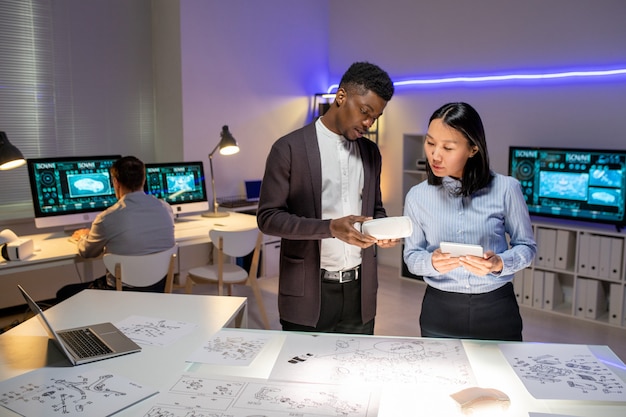 Busy multi-ethnic vehicle designers standing with maquette and tablet and working on new model of car in modern office