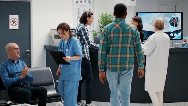 Photo busy reception desk with many patients waiting to attend consultation, trying to write medical report in hospital lobby. diverse people having appointments in waiting room area.