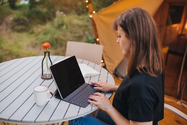 Occupato donna freelance che utilizza un laptop su un'accogliente tenda glamping in una giornata di sole tenda da campeggio di lusso per vacanze estive all'aperto e vacanze concetto di stile di vita