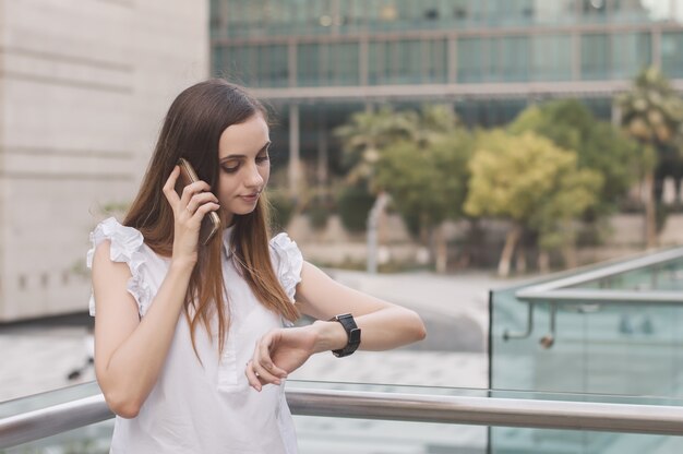 Busy woman talking via a mobile phone and looking at watches on her wrist