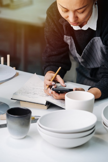 Busy woman working behind the table with newly produced blank tableware and tools