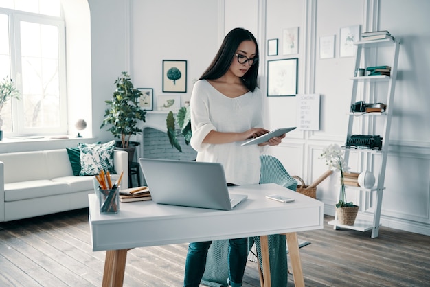 Busy working day. Beautiful young woman using digital tablet while working in home office