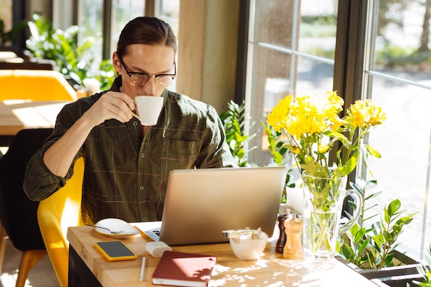 Busy working day. Serious handsome man drinking a cup of coffee while concentrating on his work