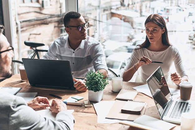 Photo busy working day. top view of young modern people in smart casual wear discussing business while sitting in the creative office