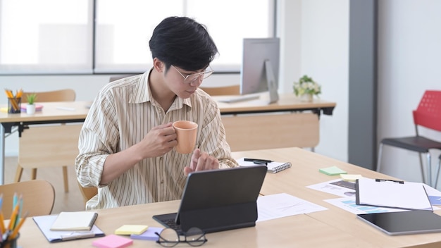 Busy young businessman drinking coffee and checking financial information on computer tablet