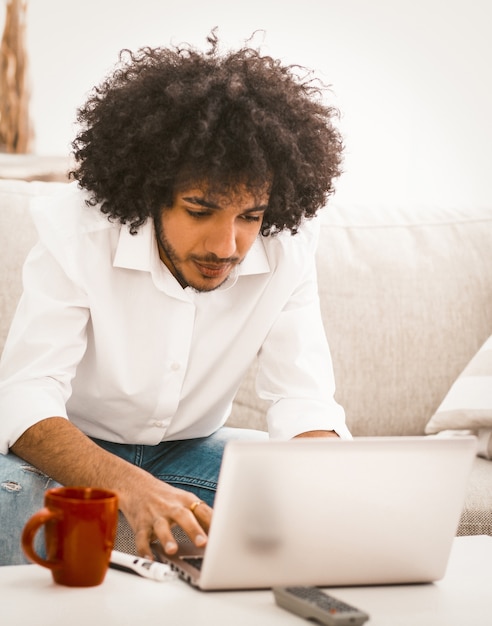 Busy young businessman typing on computer. Arabic man work from home sitting at coffee table with red cup on it. Freelance concept. Toned image