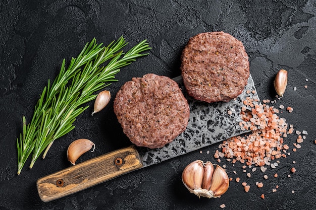 Butcher beef meat steak patties on a cleaver. Black background. Top view.