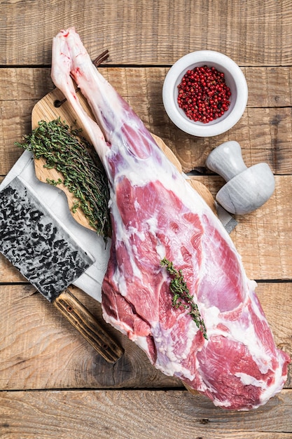 Butcher board with raw lamb mutton leg with herbs wooden\
background top view