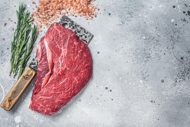 Butcher board with raw prime beef steak top sirloin or rump with pink salt and rosemary Gray background Top view Copy space