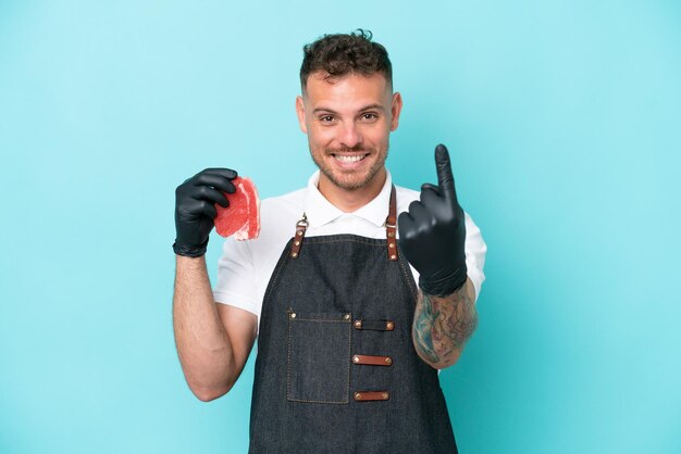 Butcher caucasian man wearing an apron and serving fresh cut meat isolated on blue background doing coming gesture