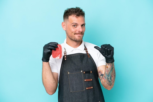 Butcher caucasian man wearing an apron and serving fresh cut meat isolated on blue background proud and selfsatisfied