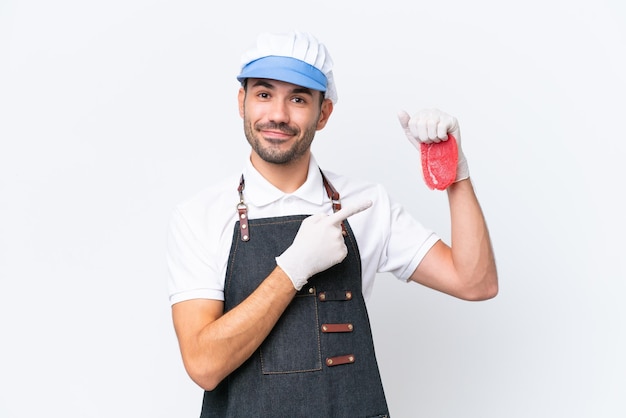 Butcher caucasian man wearing an apron and serving fresh cut meat over isolated white background pointing to the side to present a product