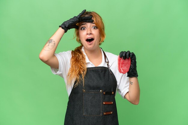 Butcher caucasian woman wearing an apron and serving fresh cut meat isolated on green screen chroma key background with surprise expression