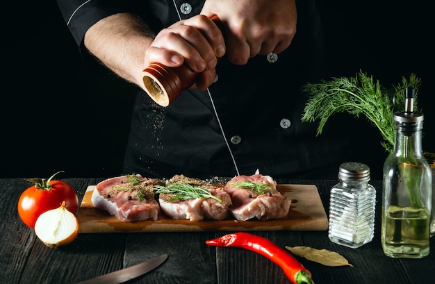 Macellaio che cucina filetto di carne e aggiunge sale, pepe e peperoncino per la marinata su sfondo nero