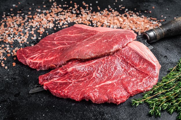 Butcher choise beef raw steaks on butcher knife Black background Top view