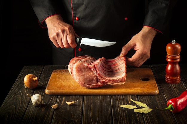 A butcher cuts raw ribs on a cutting board before preparing a meat dish