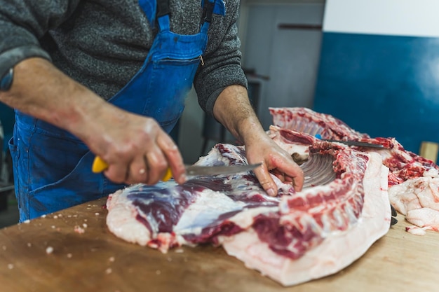 Butcher cutting raw meat of a pig with a knife at the slaughterhouse