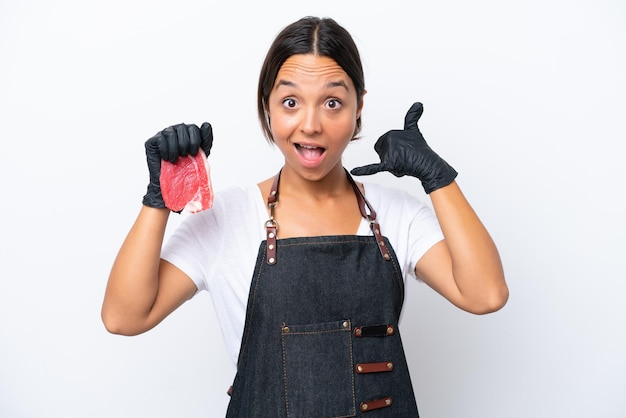 肉屋のヒスパニック系女性エプロンを着て、電話ジェスチャーを作る白い背景に分離された新鮮なカット肉を提供