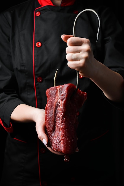 A butcher holds a piece of veal on a metal hook Meat preparation On a black background