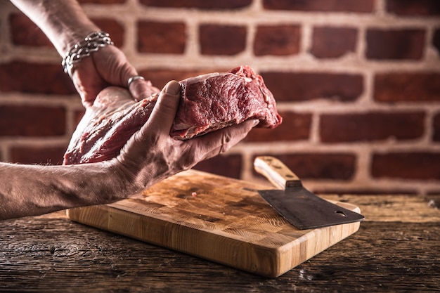 Butcher man hands holding raw beef steak in butchery.