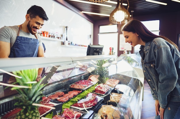 Butcher's shop seller helps to choose product to woman customer, close up