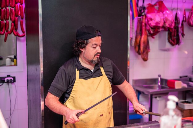 Butcher Sharpening Knife Behind Butcher Shop Counter in Yellow Apron