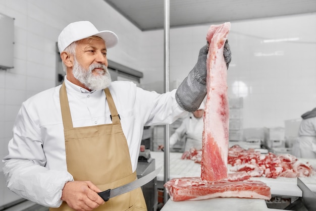 Butcher in uniform holding piece of meat and knife.