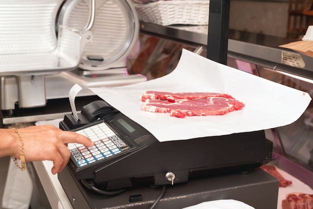 Photo butcher weighing meat at display cabinet in the butchery