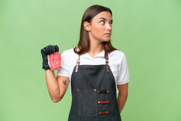 Photo butcher woman wearing an apron and serving fresh cut meat isolated on green chroma background looking to the side
