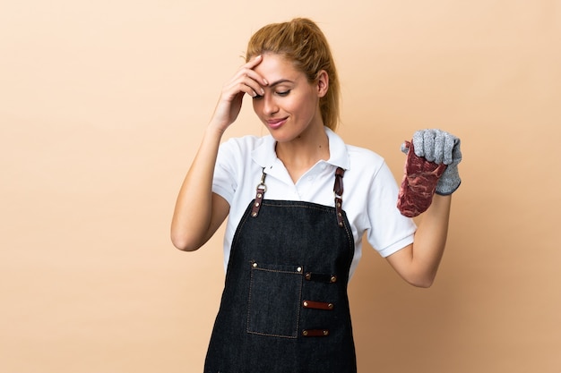 Butcher woman wearing an apron and serving fresh cut meat over isolated wall laughing