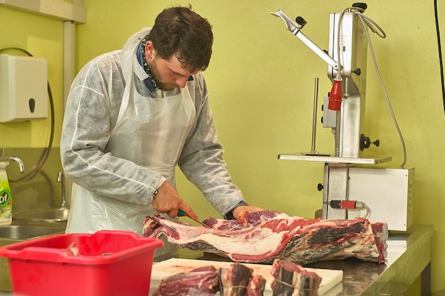 Macellaio al lavoro prepara i tagli di carne al banco e con gli attrezzi del mestiere