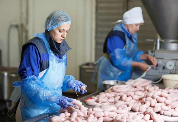 Butchers processing sausages at meat factory.