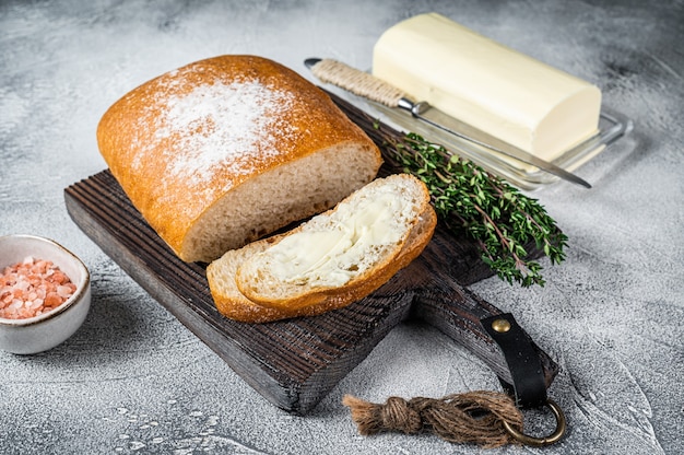 Butter block and sliced toasts of bread on a wooden board with herbs