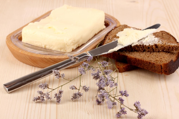 Butter on wooden holder and bread on wooden table closeup