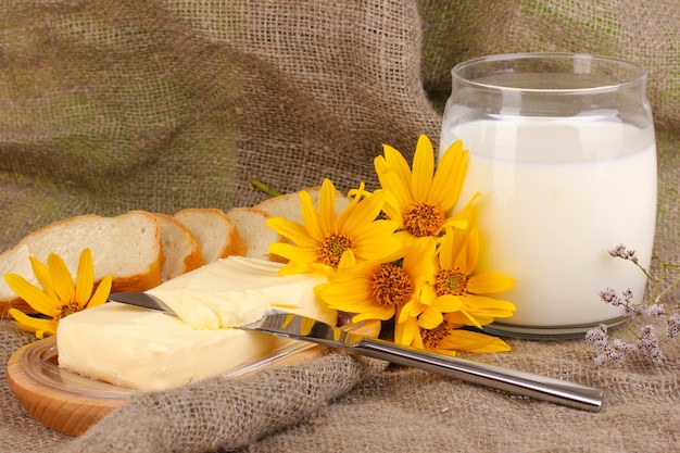 Butter on wooden holder surrounded by bread and milk on sacking background