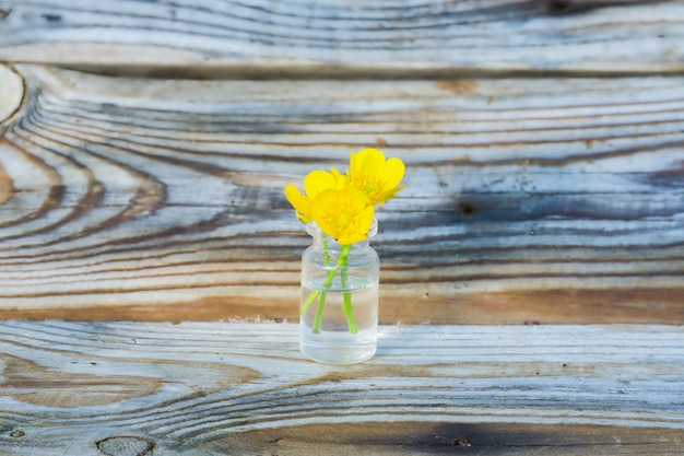 Buttercups in a small glass jar on the background of old boards.