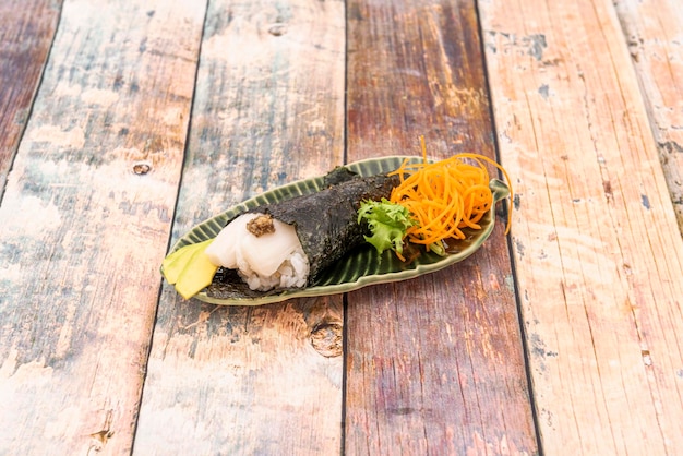 Butterfish temaki sushi with fish roe rice with rice vinegar slices of ripe avocado and nori seaweed cone on a leafshaped plate