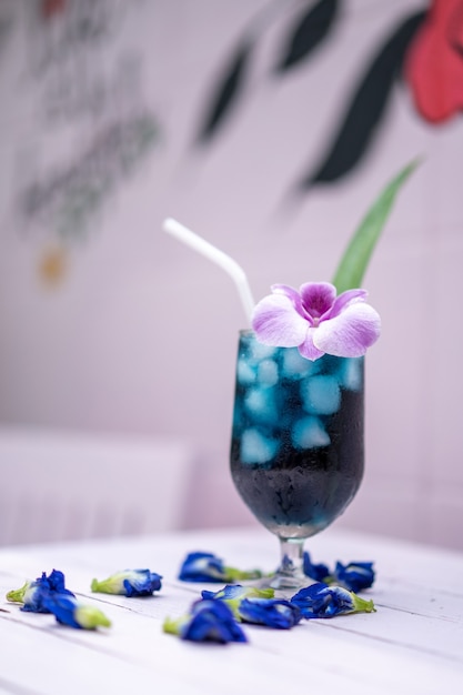 Butterfly pea on pastel pink wood table in front of cement wall at outdoor field decoration with purple orchid and pandan leaf.