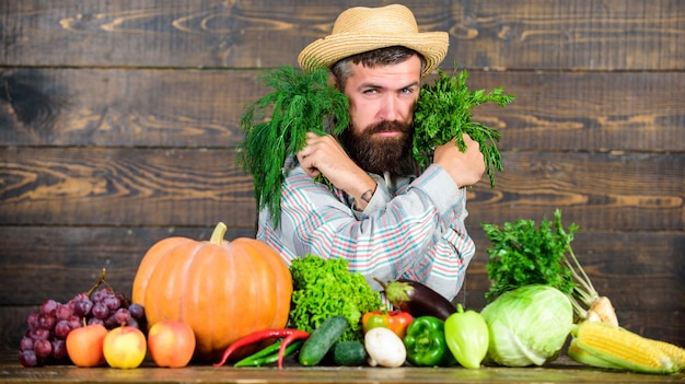 Buy fresh homegrown vegetables. Excellent quality vegetables. Man with beard proud of his harvest vegetables wooden background. Farmer with organic vegetables. Just from garden. Grocery shop concept.